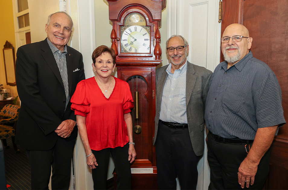 FOUR PEOPLE STANDING IN FRONT OF A GRANDFATHER CLOCK