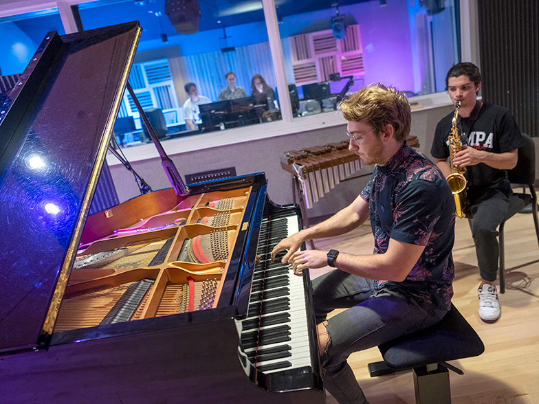 Student playing the piano while a student is playing saxaphone.