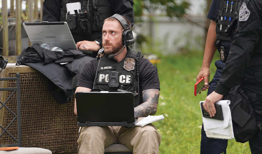 Police officer sits with computer  on lap outdoors