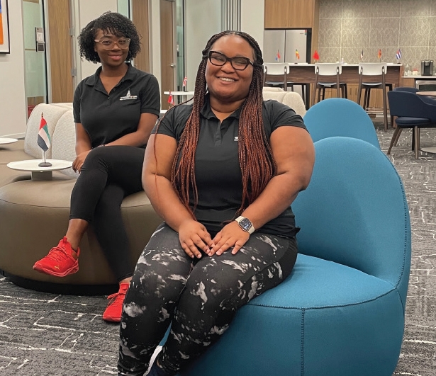 TWO WOMEN ARE SEATED, SMILING AT THE CAMERA