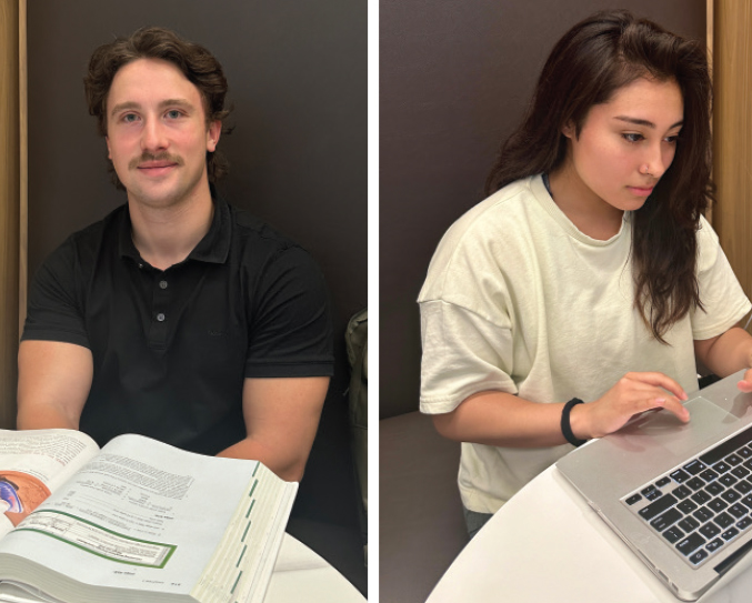 A MAN WITH A MOUSTACHE WEARING A BLACK SITS ATA TABLE WITH AN OPEN BOOK IN FRONT OF HIM and A WOMAN WITH LONG, DARK HAIR WORKS ON A LAPTOP COMPUTER