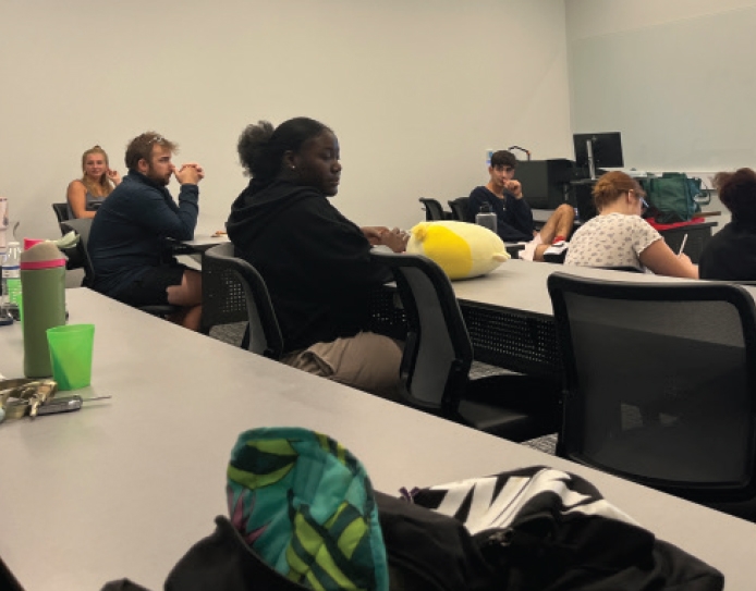 SEVERAL PEOPLE ARE SEATED AT LONG TABLES IN A CLASSROOM