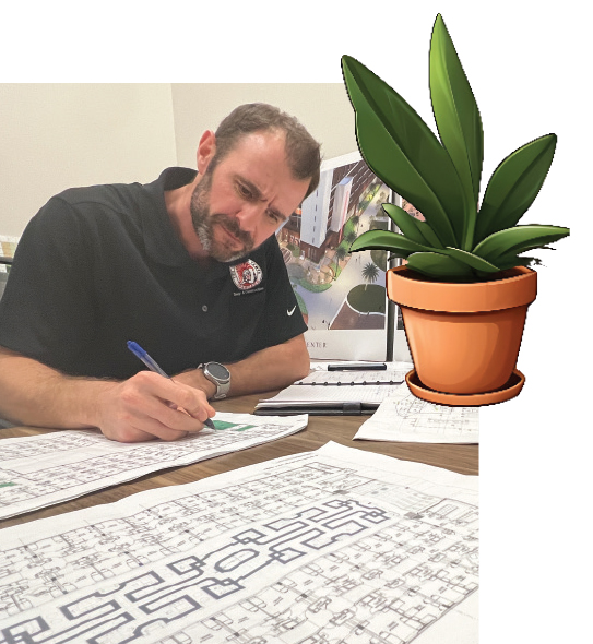 A MAN AT A DESK WORKS ON ARCHITECTURAL DRAWINGS with an AN ILLUSTRATION OF A POTTED PLANT