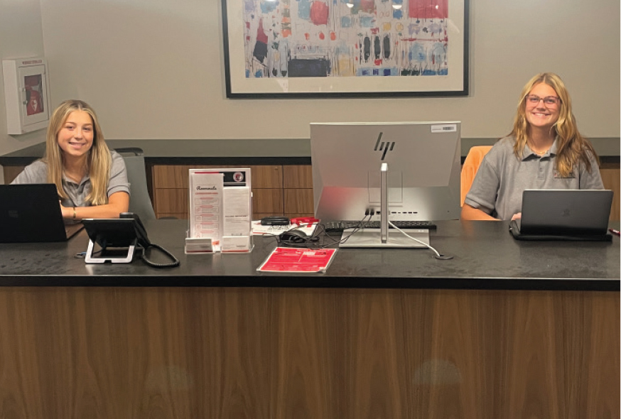 TWO WOMEN ARE SEATED AT A RECEPTION DESK