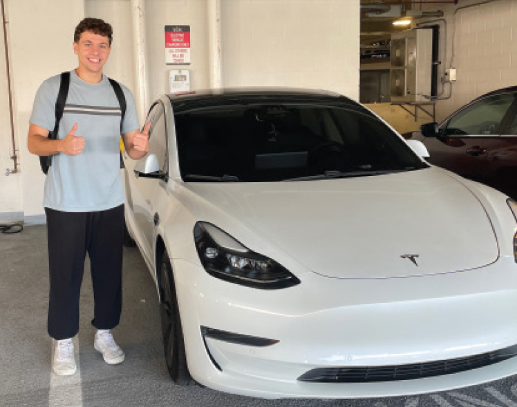 A MAN GIVING THE THUMBS-UP SIGN STANDS NEAR A CAR IN A PARKING GARAGE