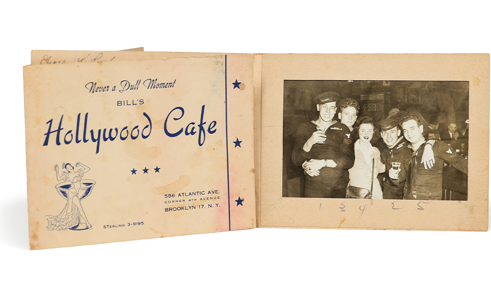 A black and white photo of five people at a bar, smiling at the camera.