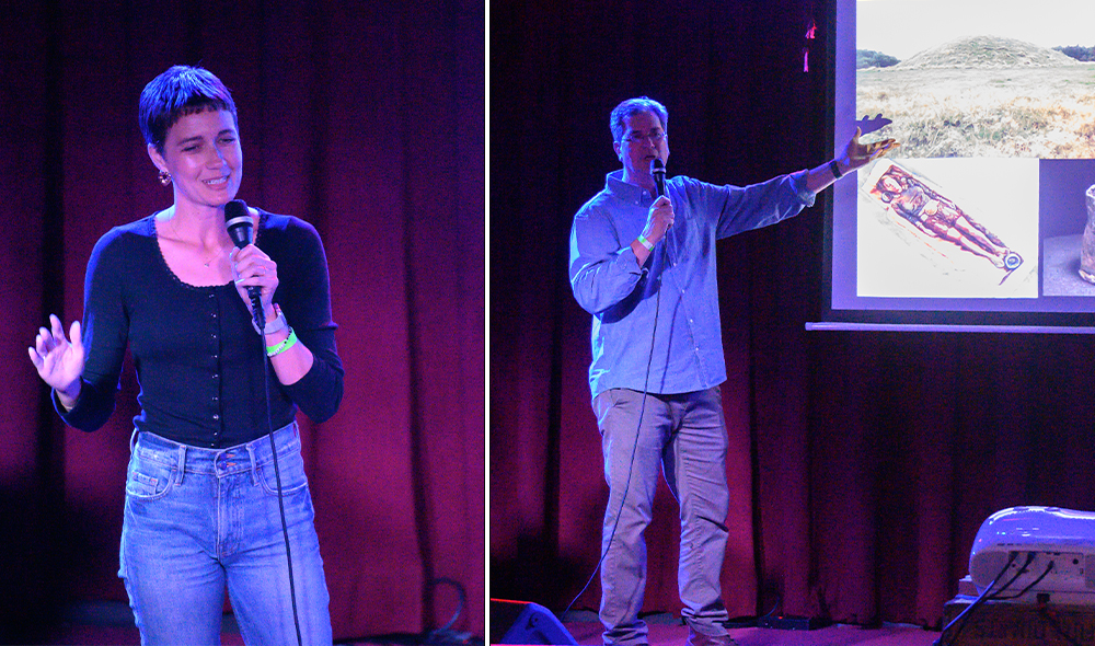A woman stands, holding a microphone and A man stands with a microphone, gesturing toward a presentation screen.