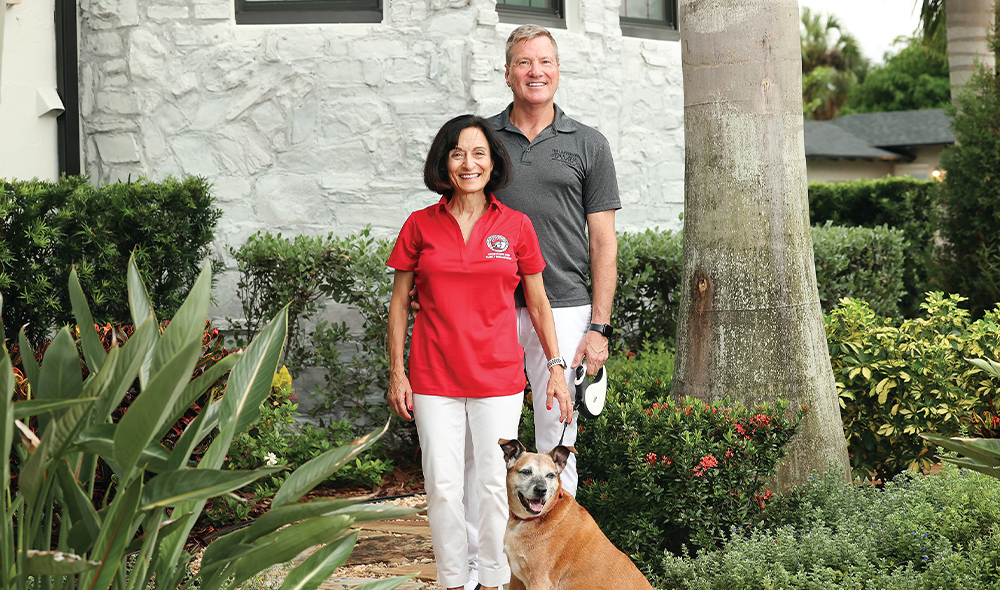 A WOMAN AND A MAN STAND BY A TREE WITH A DOG