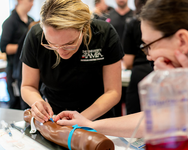 Woman learning how to draw blood from a dummy model.
