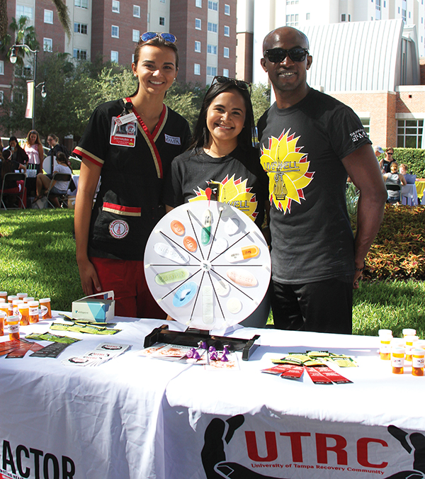Three students promote Live Well UT outside at a table. 