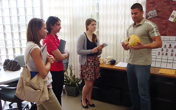 Three students watch a professor as he reviews a model skull.