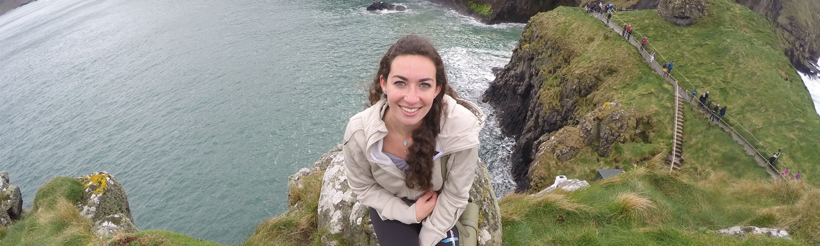 Student smiling, posing on a cliff overlooking water