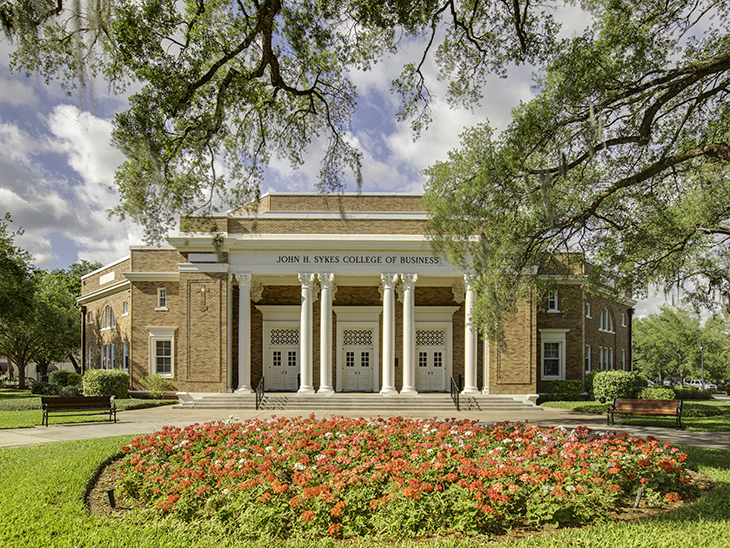 Sykes College of Business framed by flowers and an oak tree