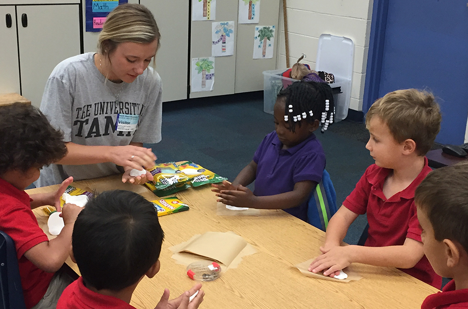 Lauren Kulick at a table with several young children, teaching a science lesson.